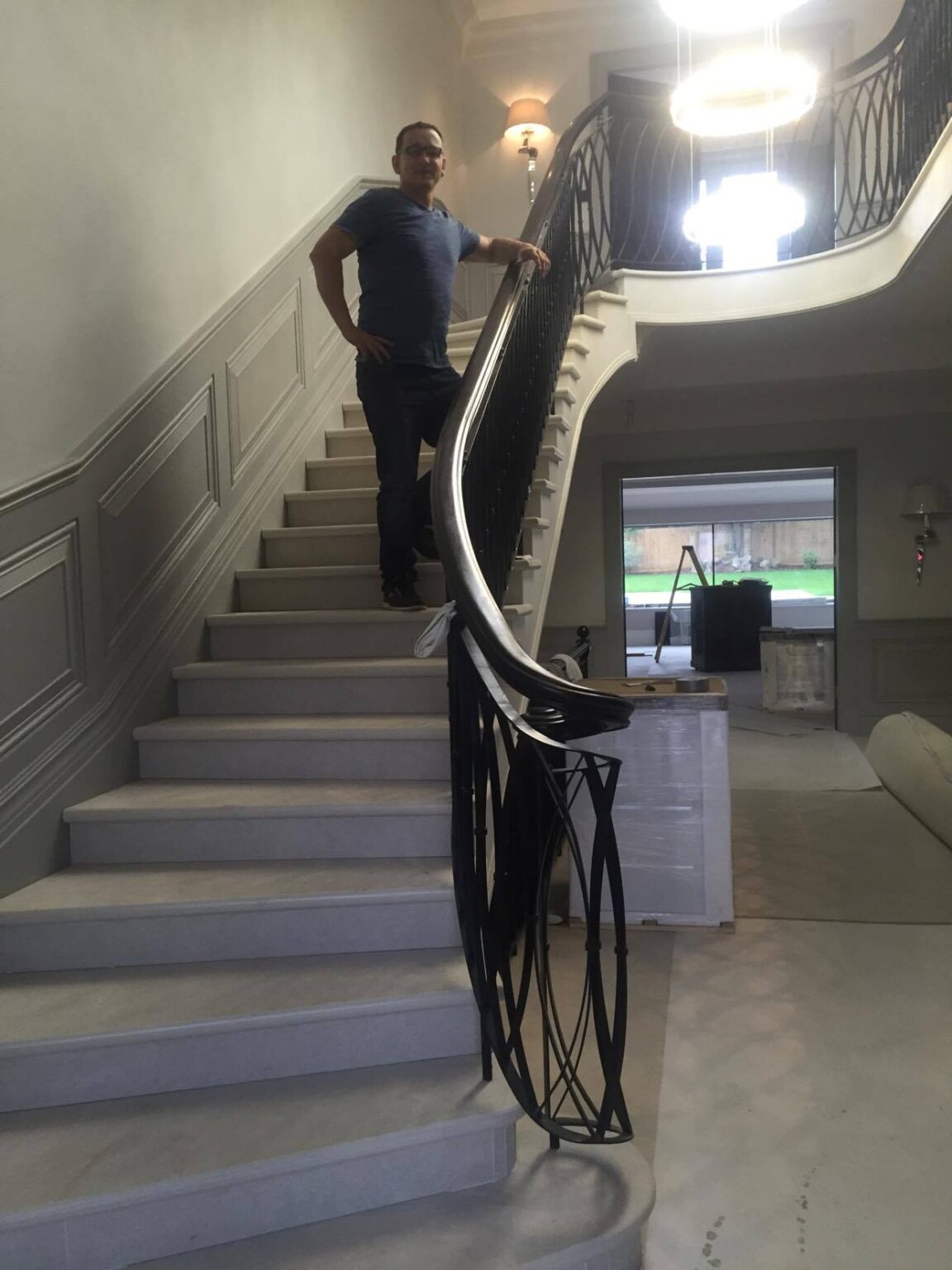 A person standing on an interior staircase with pale finishes and a curved black metal balustrade